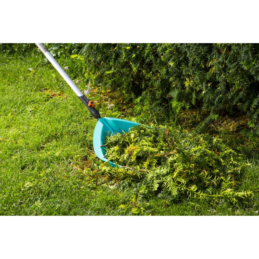 Person sammelt Gartenabfälle mit Schaufelrechen.