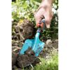 Hand benutzt einen Handgrubber im Garten.