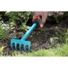 Hand harkt mit kleiner Harke Erde im Garten