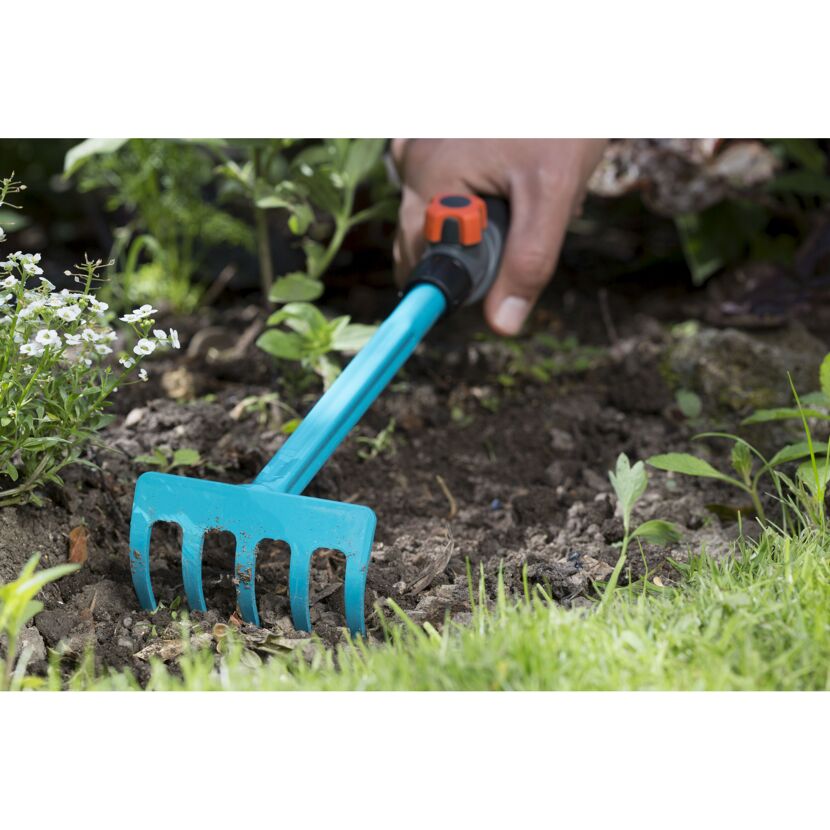 Hand harkt mit kleiner Harke Erde im Garten