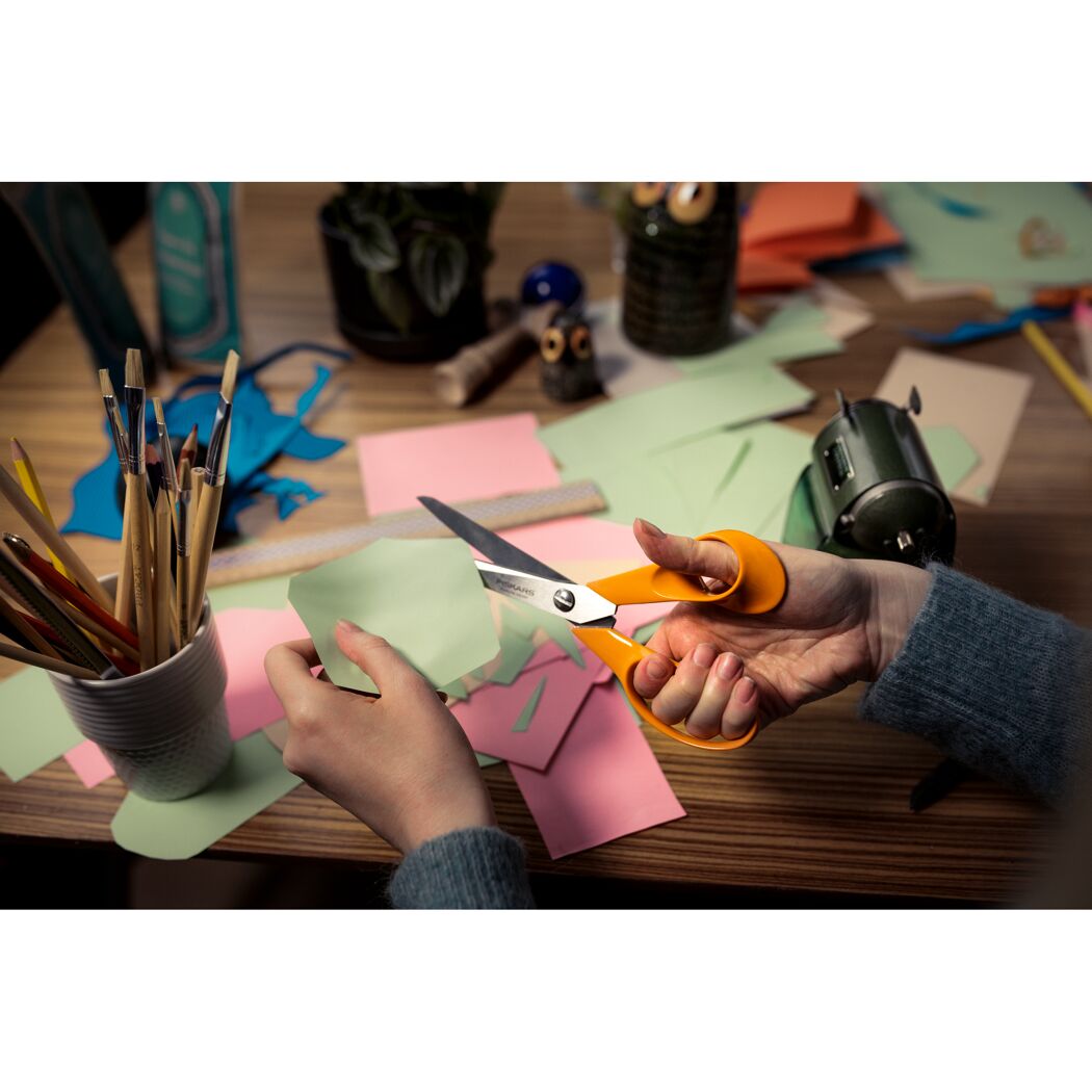Person schneidet Papier mit orangefarbener Fiskars Schere