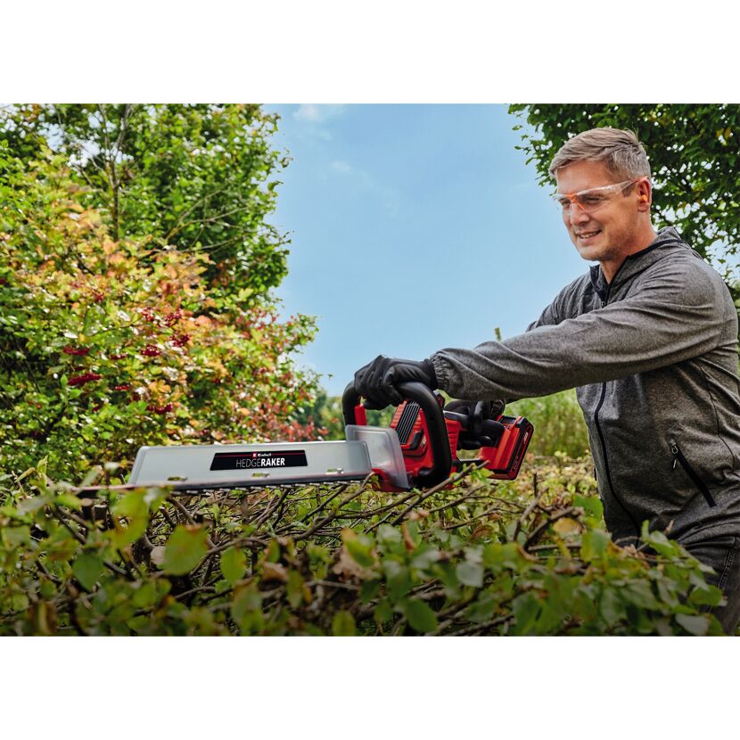 Person verwendet Heckenschere zum Schneiden einer Hecke.