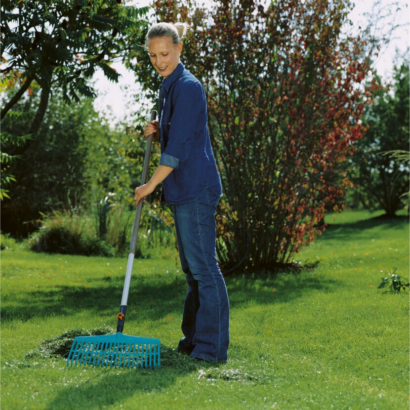 Person rechnet mit einem Rechen Laub im Garten zusammen.