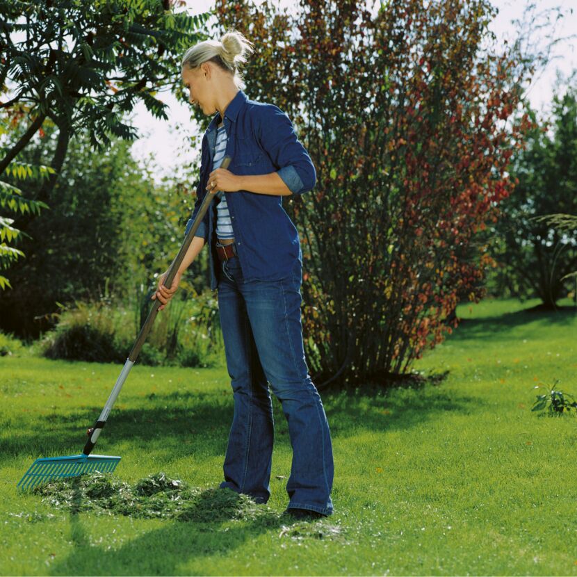 Person rechnet mit Rechen Laub im Garten zusammen.