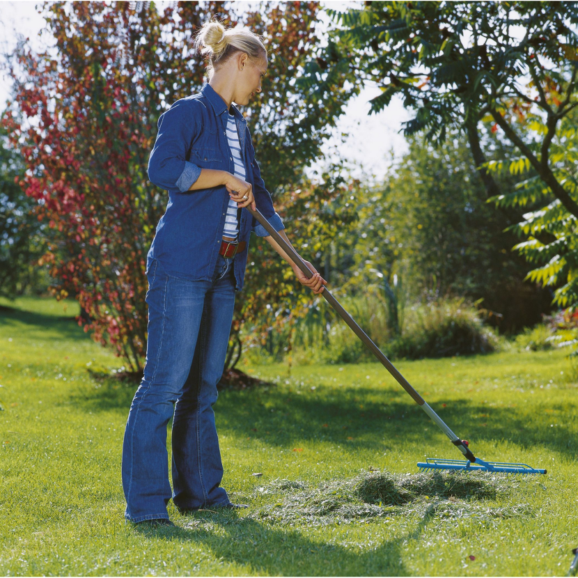 Person rechnet mit einem Rechen Gras im Garten zusammen.