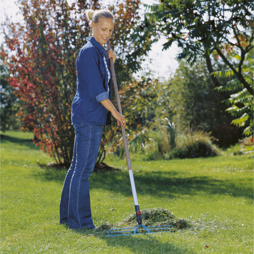 Person rechnet mit einem Rechen Gras im Garten zusammen.