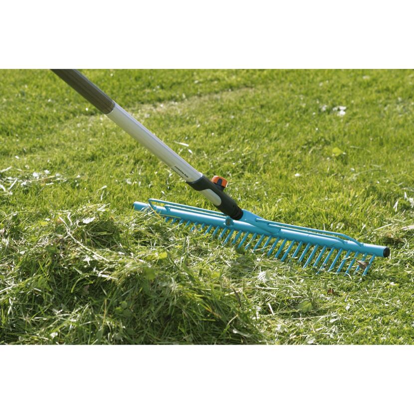 Person rechnet mit einem blauen Rasenrechen Gras zusammen.