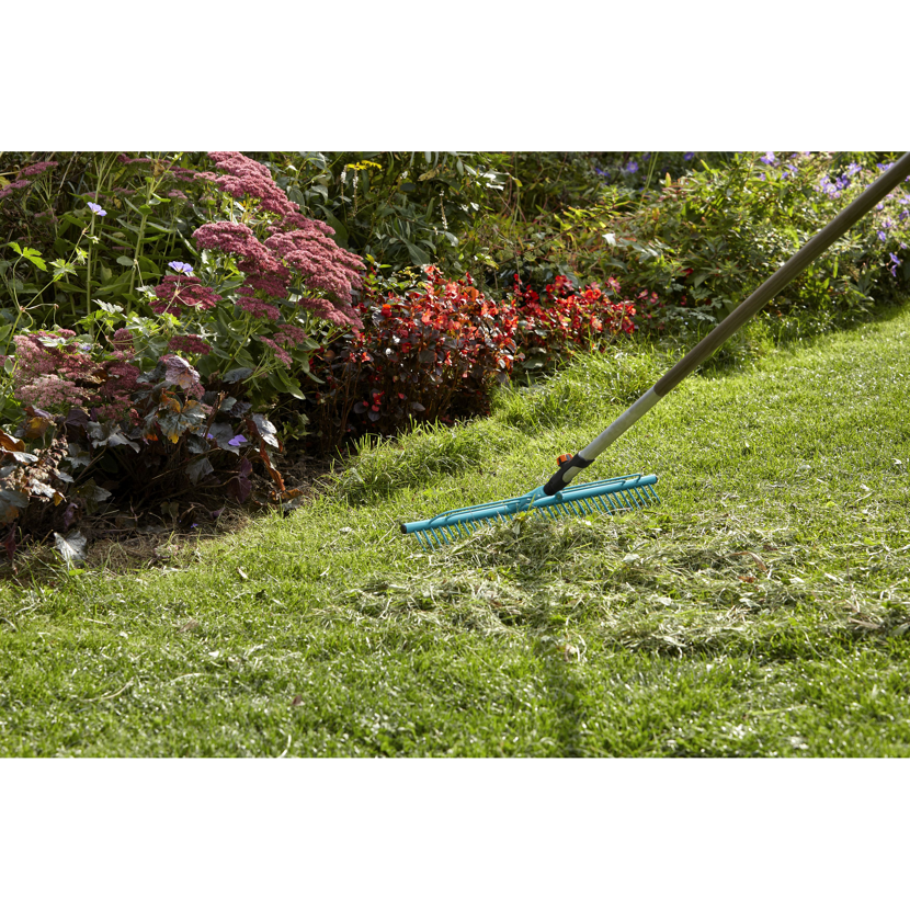 Person harkt mit einem Rechen Laub im Garten zusammen.