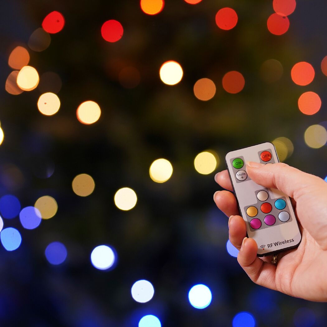 Person drückt Knopf auf Fernbedienung für bunte Lichterkette