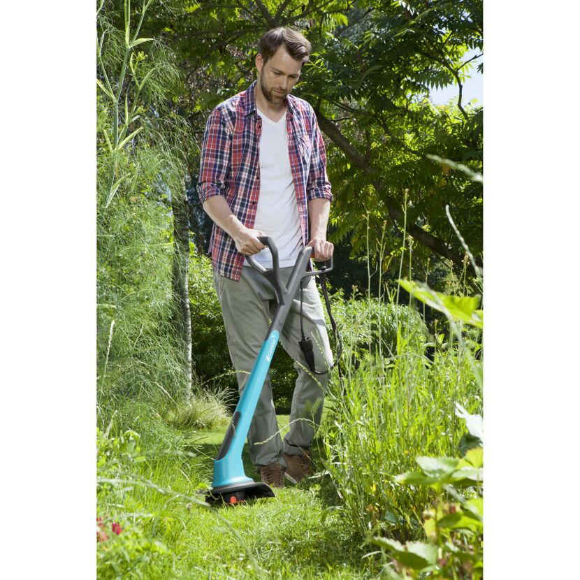 Person verwendet elektrischen Rasentrimmer im Garten.