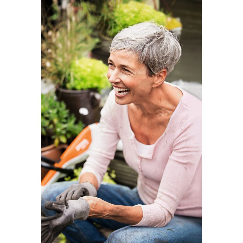 Person zieht Gartenhandschuhe an und lacht.