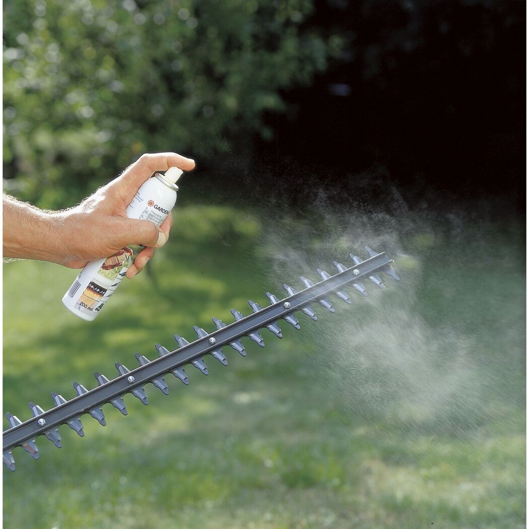 Person sprüht Pflegespray auf Heckenschere