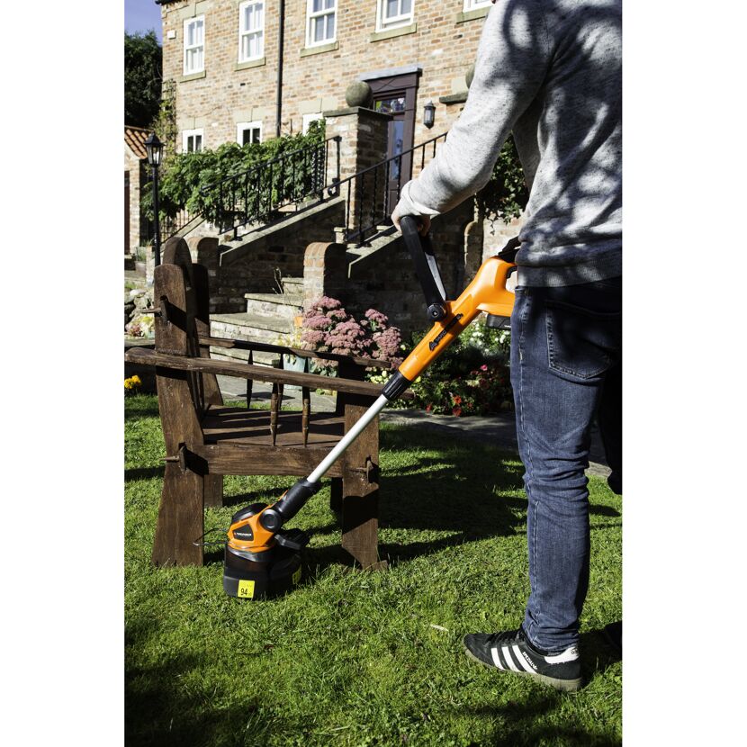 Person verwendet einen Akku-Rasentrimmer im Garten.