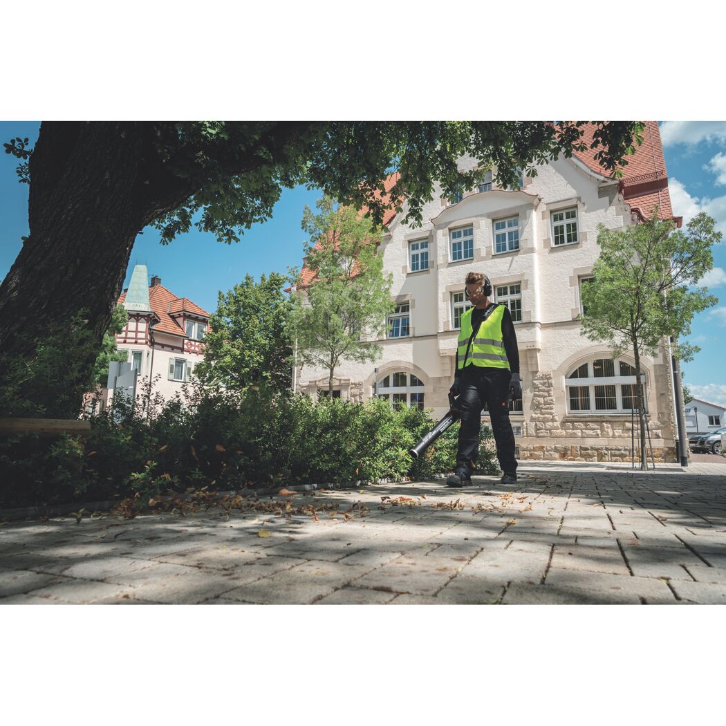 Person mit Laubbläser auf einem gepflasterten Weg.