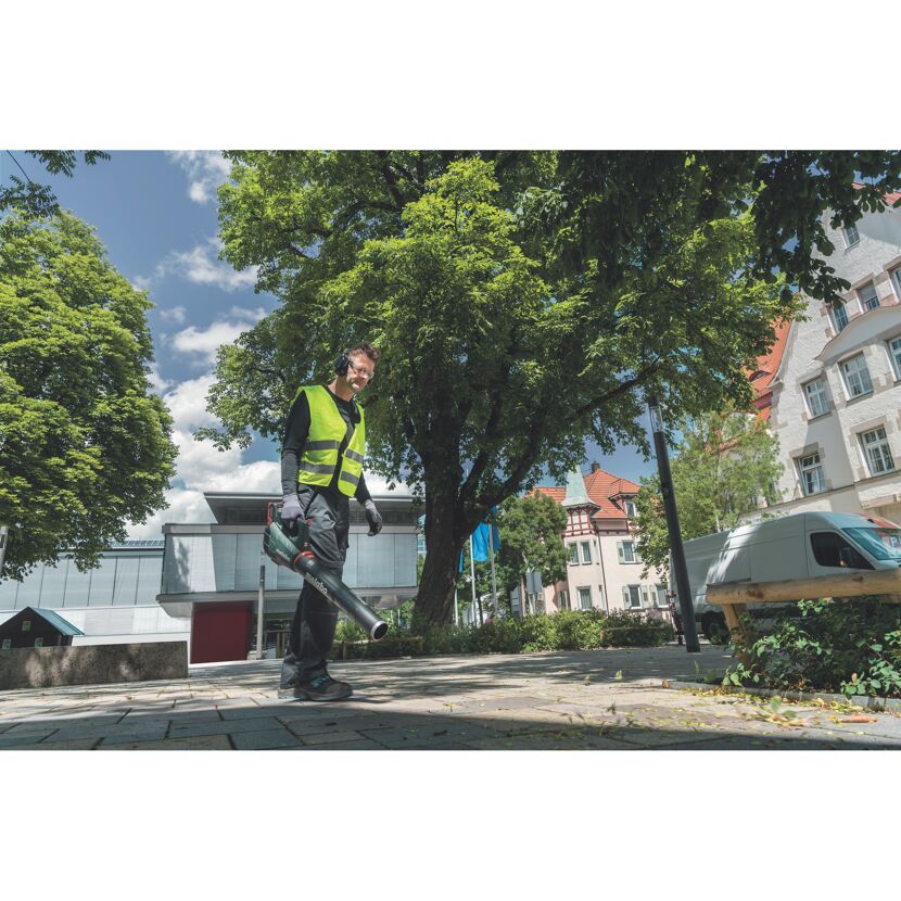 Person reinigt einen Bürgersteig mit einem Laubbläser.