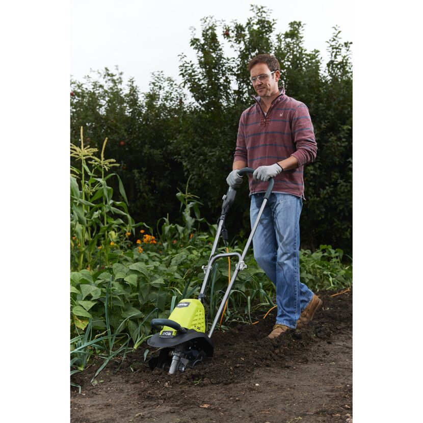 Person verwendet einen elektrischen Kultivator im Garten.