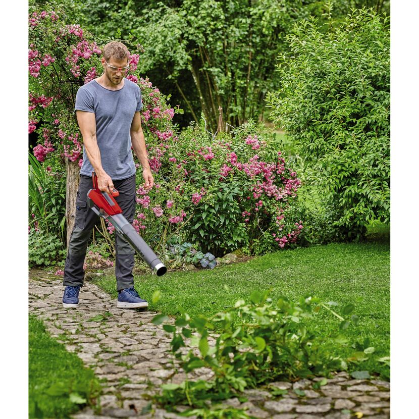 Person entfernt Laub mit Laubbläser im Garten.