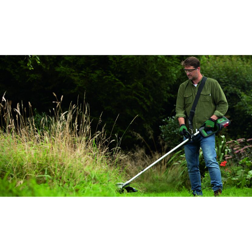 Person mäht mit einem Akku-Rasentrimmer hohes Gras.