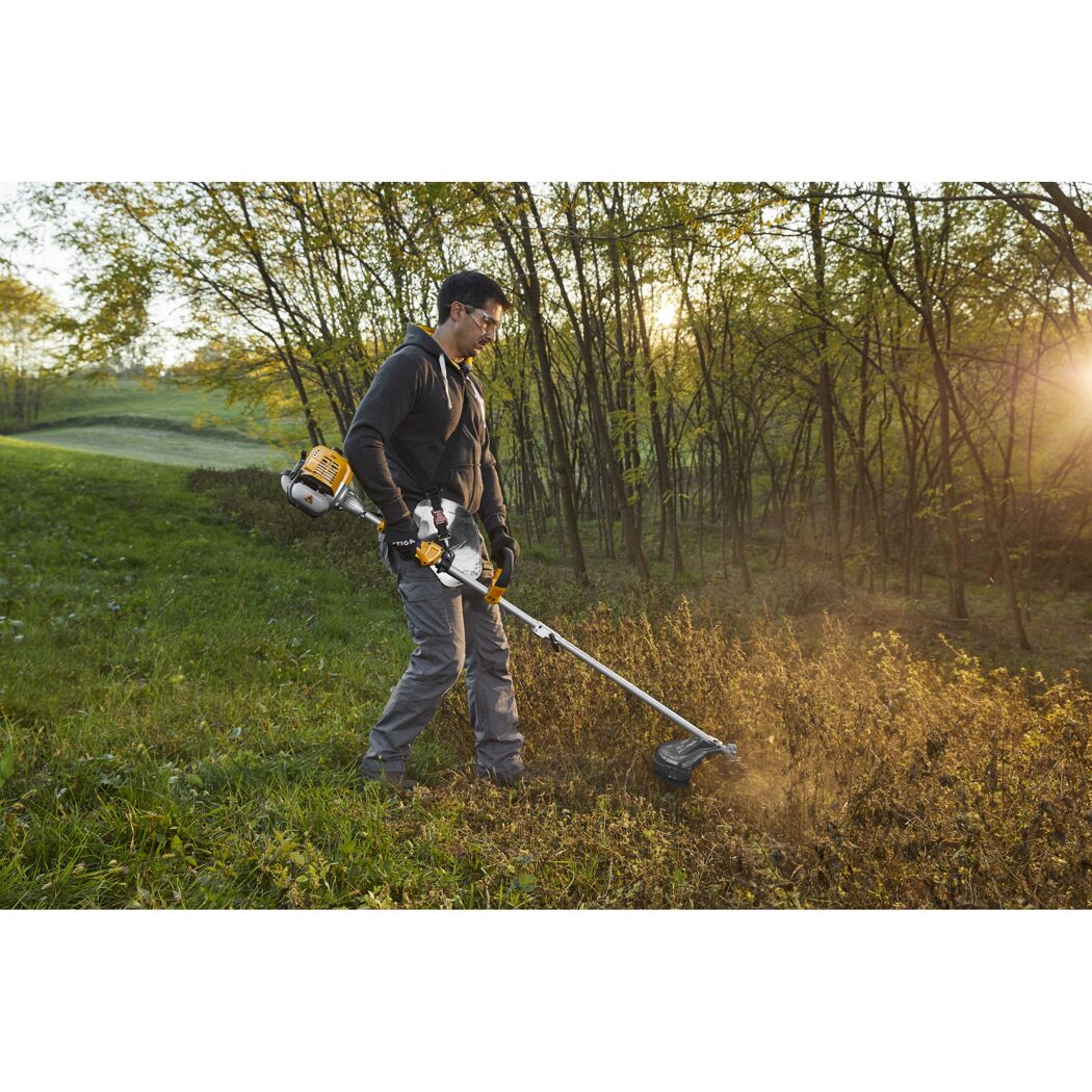 Person mäht mit Freischneider Gras am Waldrand.