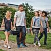 Vier Personen tragen einen Gasgrill Go-Anywhere und Picknickutensilien.