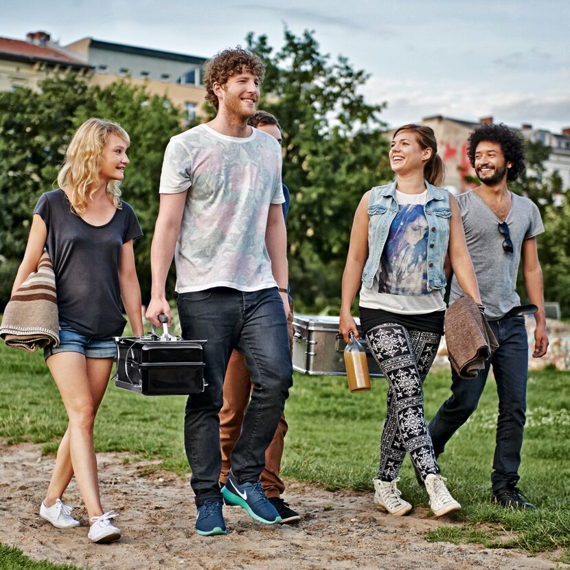 Vier Personen tragen einen Gasgrill Go-Anywhere und Picknickutensilien.