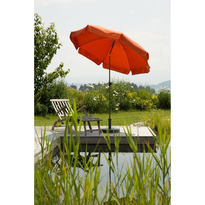 Orangener Sonnenschirm neben einem Holzliegestuhl an einem Teich.