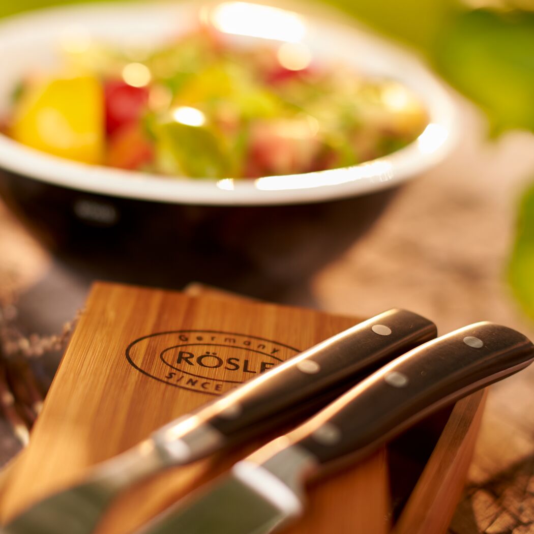Zwei Steakmesser auf einem Holzbrett. Im Hintergrund eine Schüssel Salat.