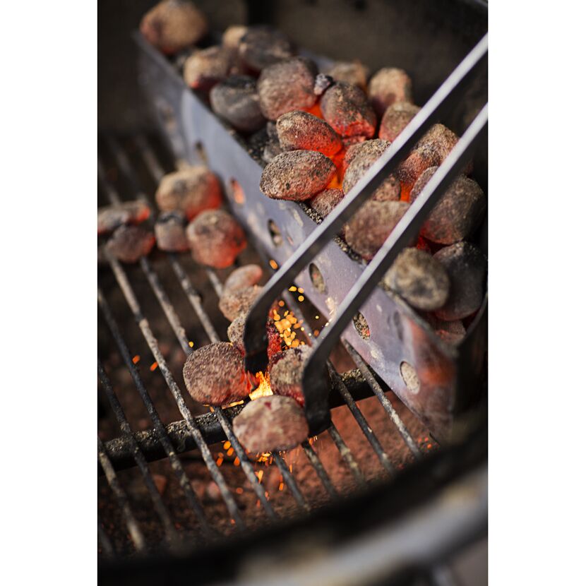 Glühende Kohlen werden mit einer Grillzange auf dem Grillrost verteilt.