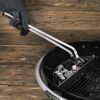 Person hält Grillzange über Holzkohlegrill