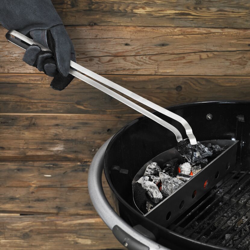 Person hält Grillzange über Holzkohlegrill