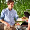 Person grillt Burger und reicht einen Burger mit Grillzange