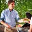 Person grillt Burger und reicht einen Burger mit Grillzange
