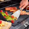Person grillt Gemüse und Würstchen mit einem Spachtel.