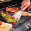 Person grillt Gemüse und Würstchen mit einem Spachtel.