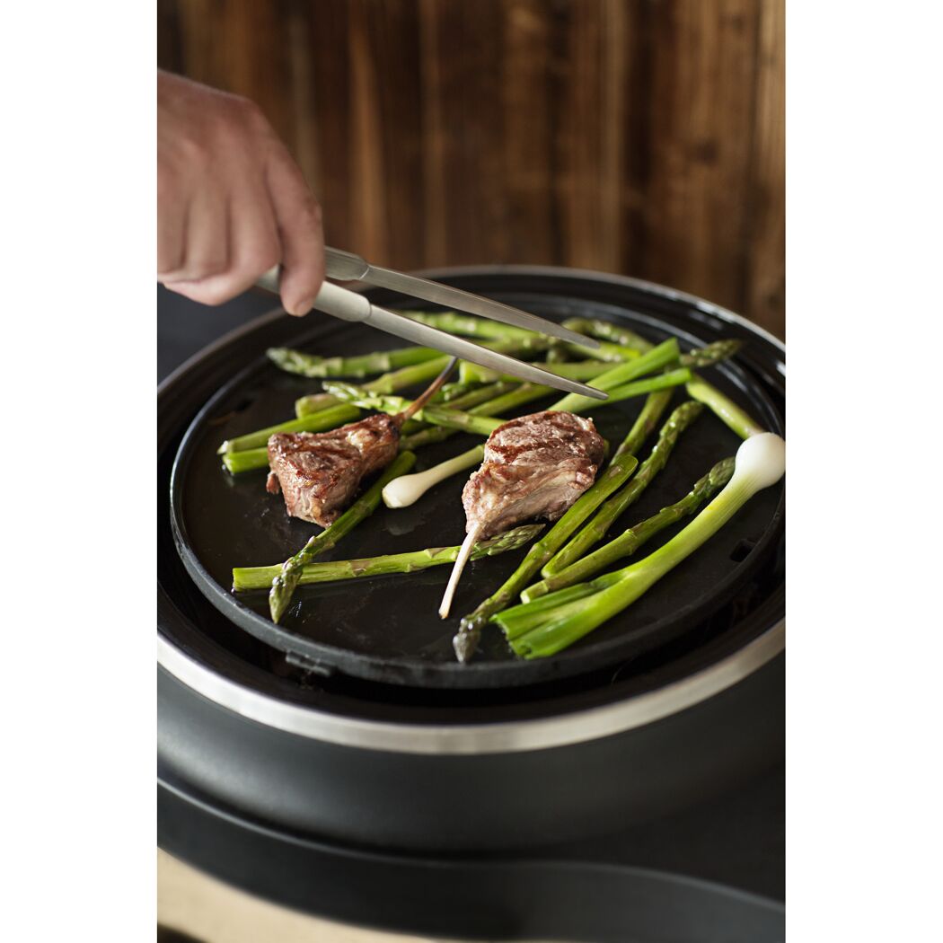 Person grillt Lammkoteletts und Spargel mit einer Zange.