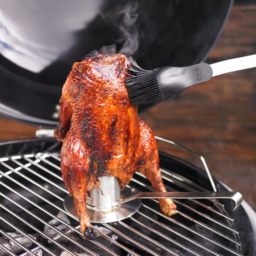 Hähnchen wird auf einem Hähnchenbräter gegrillt und mit einem Pinsel bestrichen.