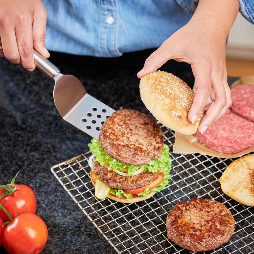 Person legt Burgerpatty mit Pfannenwender auf Burger