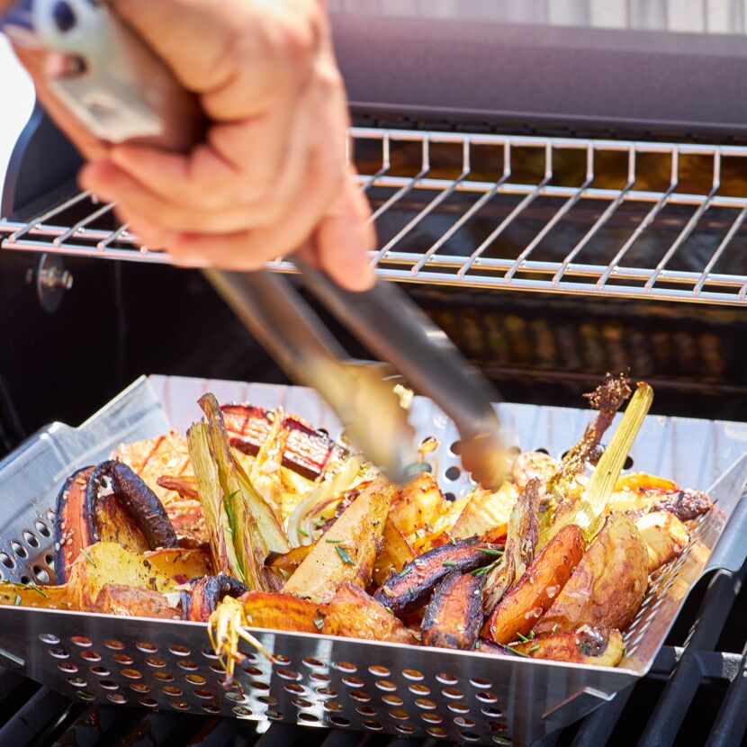 Person grillt Gemüse mit Grillzange in Grillpfanne