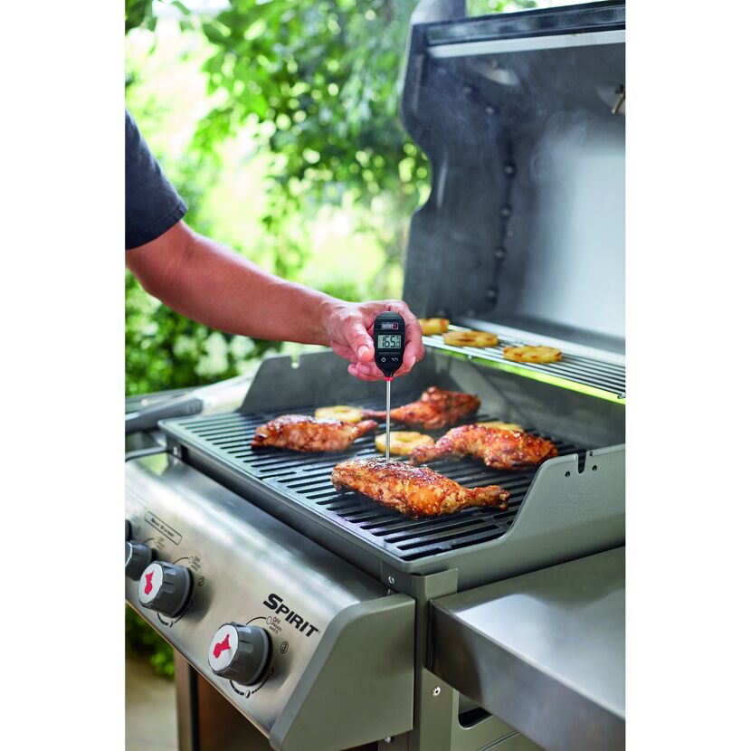 Person misst Temperatur von Hähnchen auf dem Grill mit Thermometer.