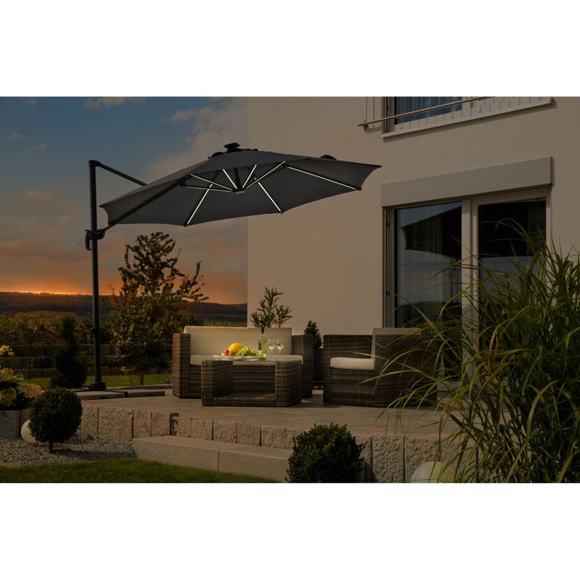 Person sitzt auf Terrasse unter geöffnetem Sonnenschirm mit Beleuchtung