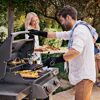 Zwei Personen grillen auf einem Gasgrill im Garten.