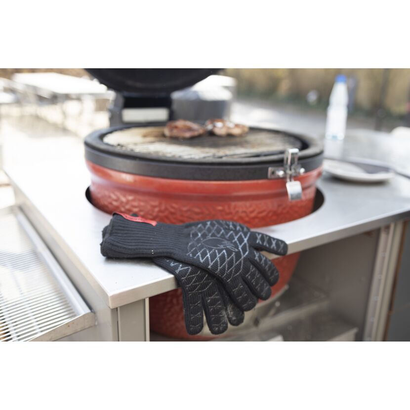 Grillhandschuhe liegen auf einem Grill, auf dem Fleisch gegrillt wird.