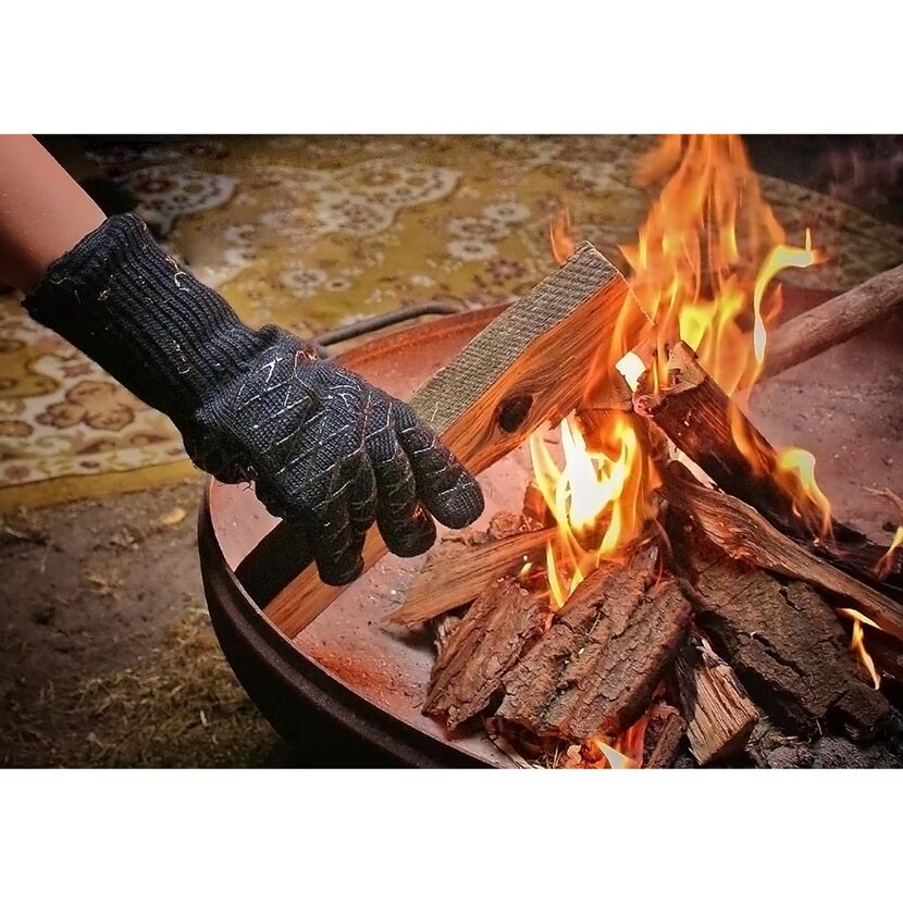Person mit Grillhandschuh legt Holzscheit ins Feuer