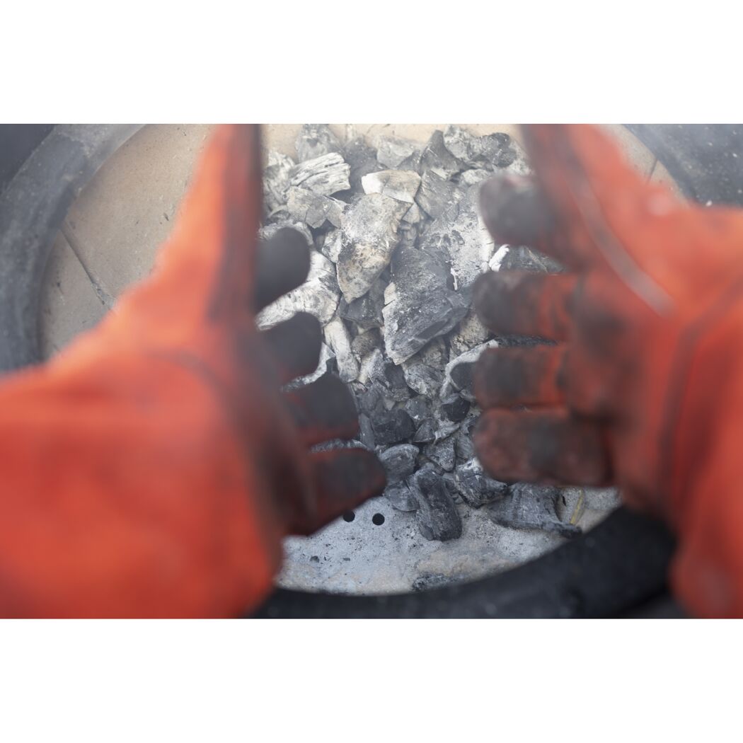 Hände mit Grillhandschuhen über einem Holzkohlegrill