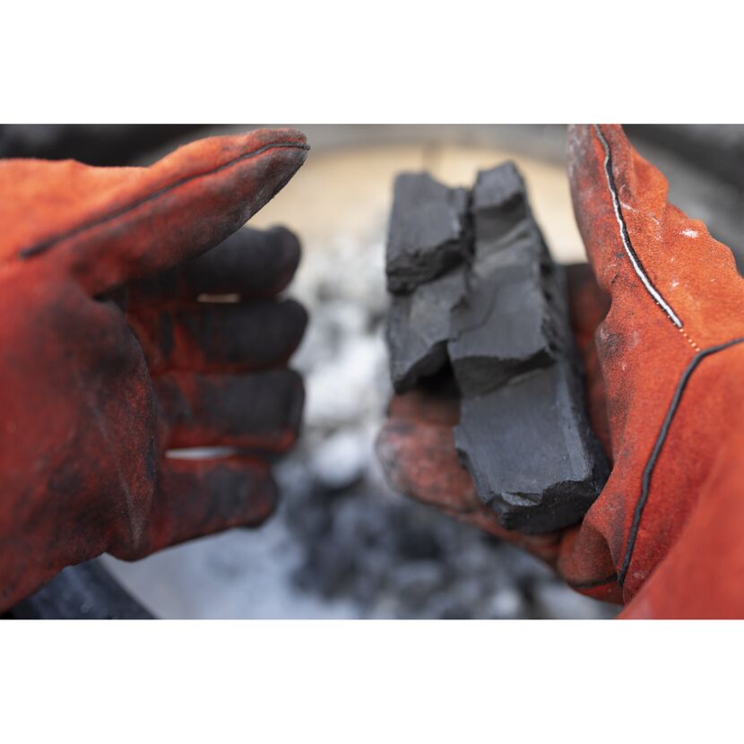 Hände mit orangefarbenen Handschuhen halten Holzkohle