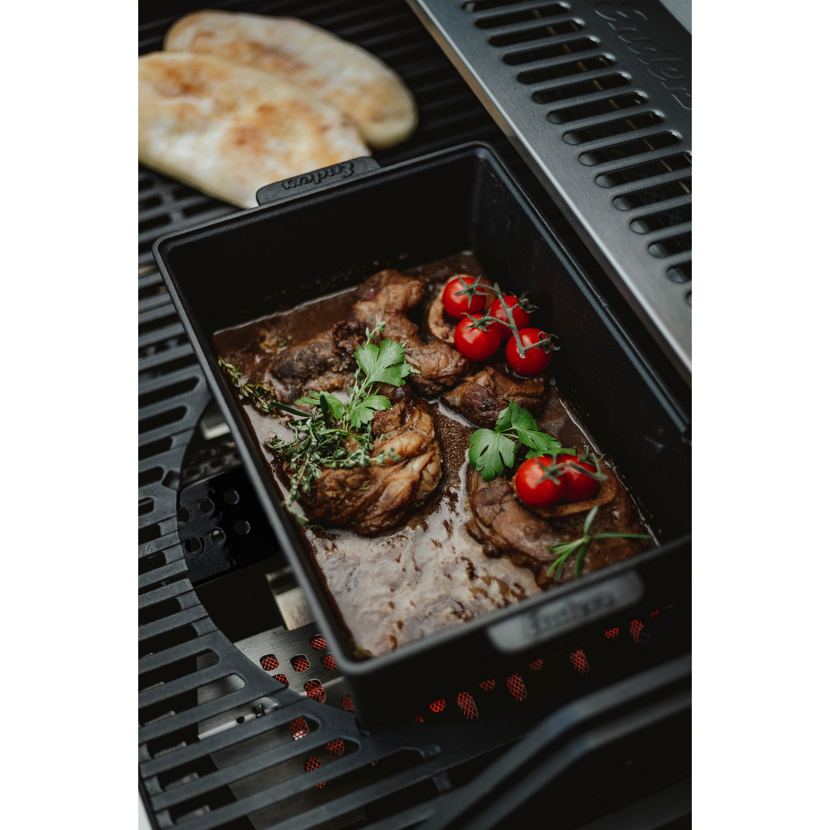 Fleisch mit Kräutern und Tomaten im gusseisernen Bräter auf dem Grill