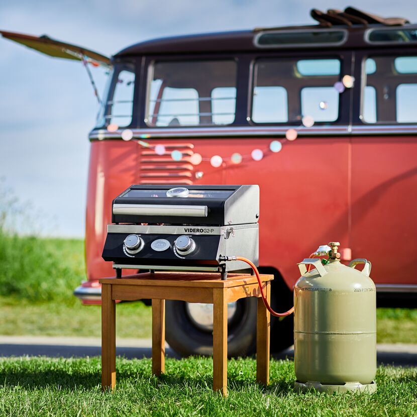 Tragbarer Gasgrill vor einem Campingbus.