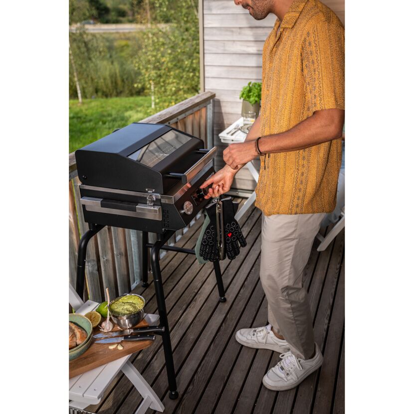 Person bedient einen schwarzen Gasgrill auf dem Balkon.