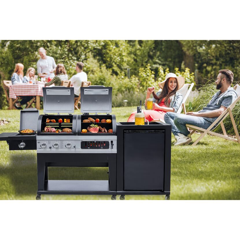 Personen sitzen im Garten und entspannen sich neben einem Gasgrill. Auf dem Grill liegen verschiedene Speisen wie Würstchen, Steaks und Maiskolben.