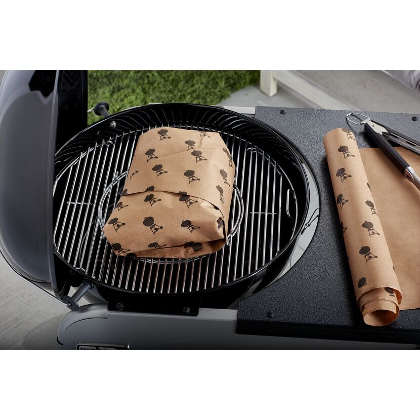 Fleisch wird in Backpapier auf einem Grill gegart.
